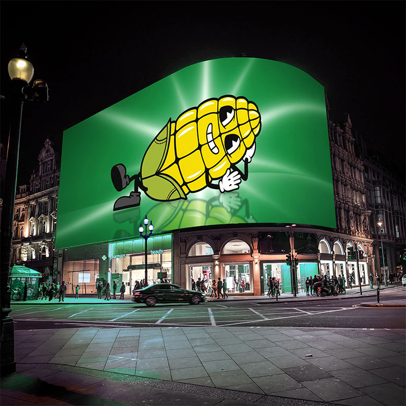 Large nighttime billboard displaying Cobbie corn character in a cheerful expression on a green background.